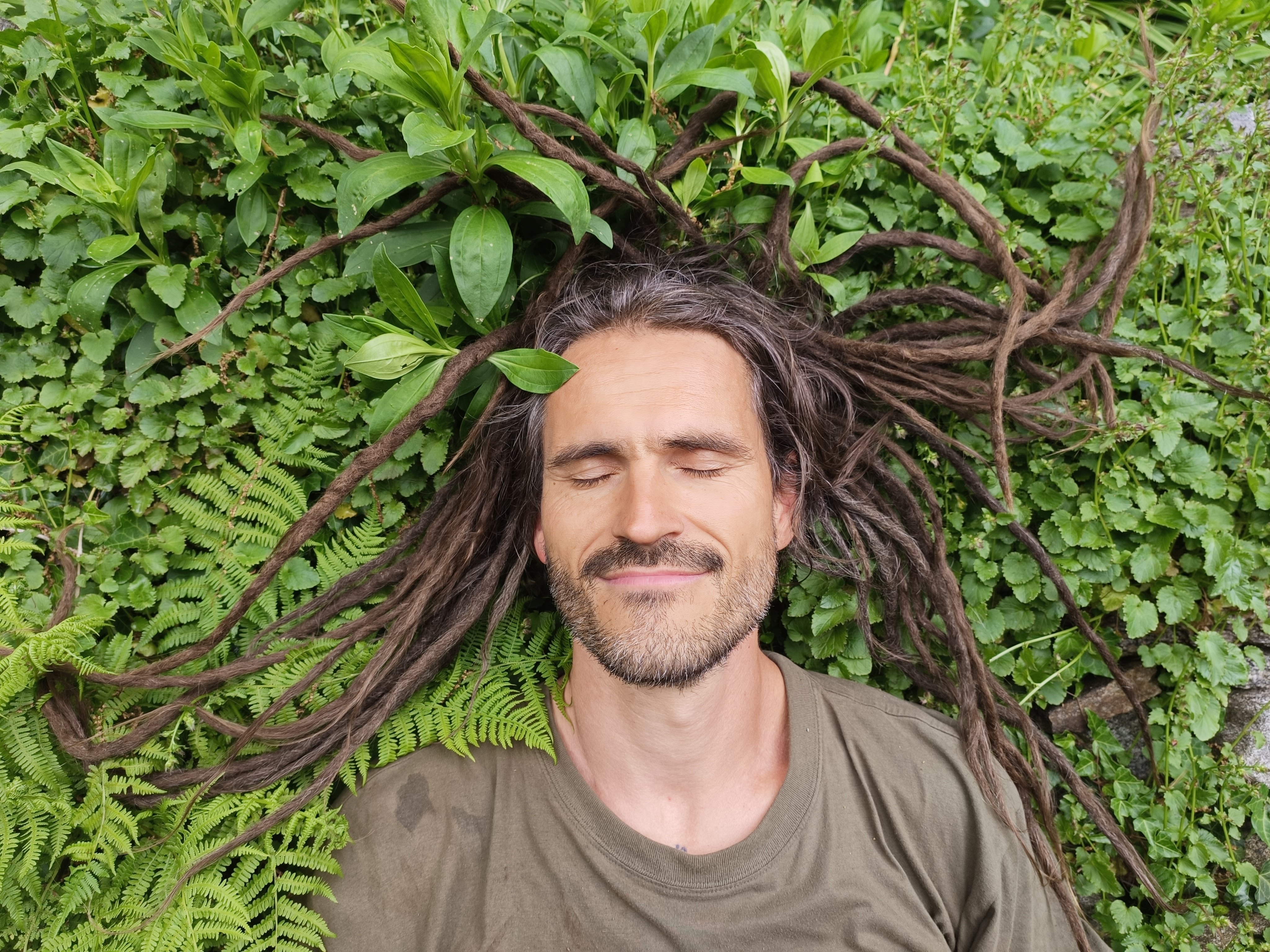 Kusi inmitten von grünen Pflanzen, mit Dreadlocks im Gras ausgebreitet